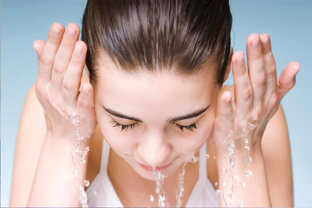 زنی در حال آب زدن و شستن صورت خود -شستن صورت پس از لیزر