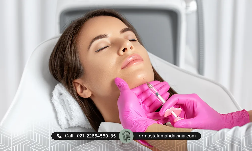 خانمی با چشمان بسته که دراز کشیده و پزشک در حال تزریق فیلر چانه می باشد. | مراقبت بعد از فیلر چانه​